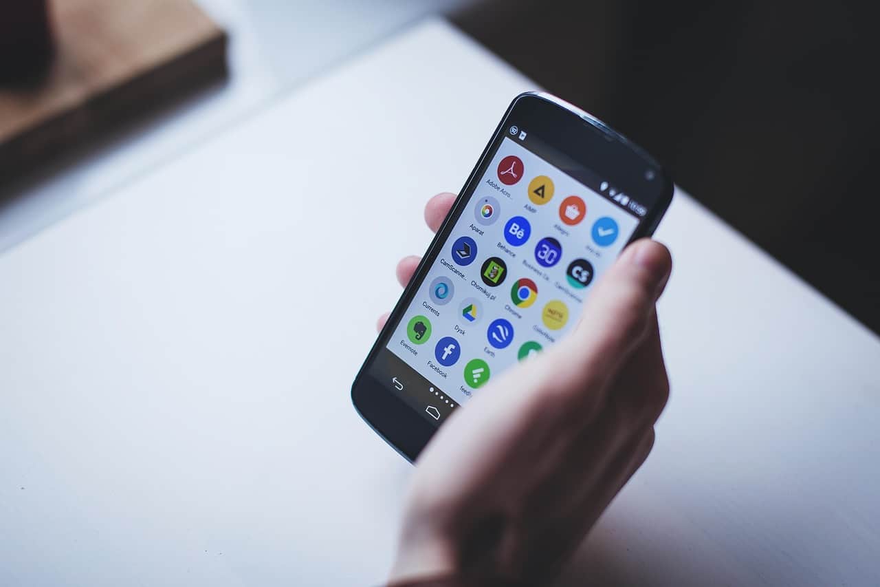 Une personne tient un smartphone affichant des icônes d'applications mobiles.