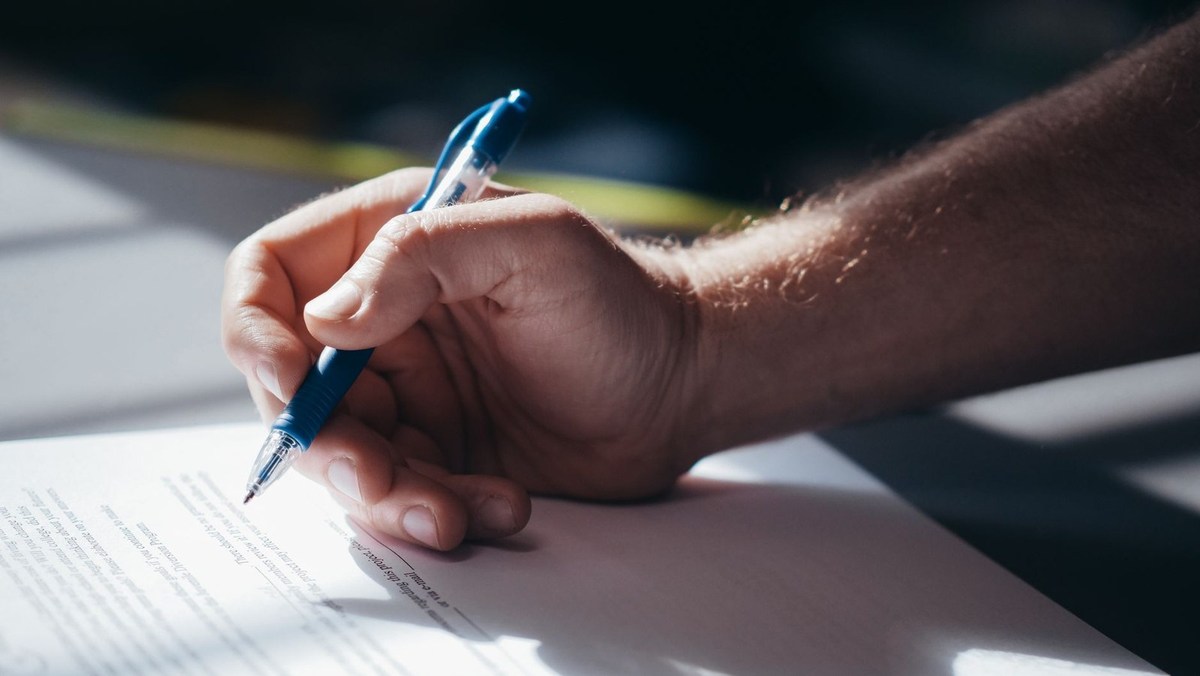 Main écrivant avec un stylo bleu sur un papier à la lumière naturelle