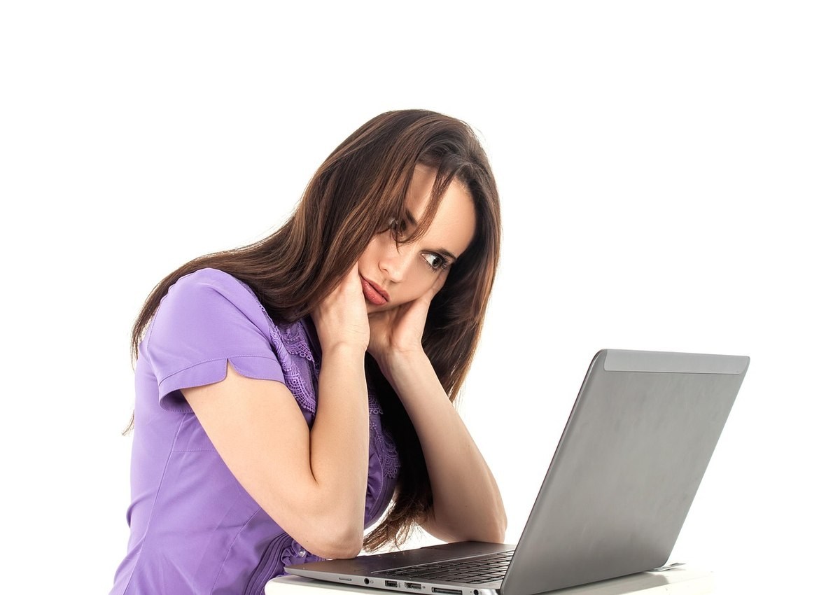 Une femme en violet repose la tête sur la main devant un ordinateur