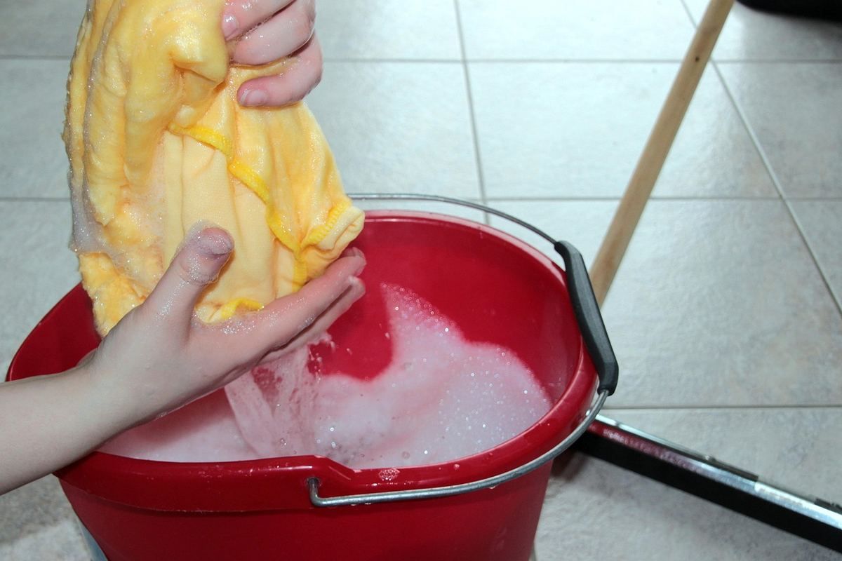 Personne plongeant un linge jaune dans un seau d'eau rouge pour le nettoyer Personne plongeant un linge jaune dans un seau d'eau rouge pour le nettoyer
