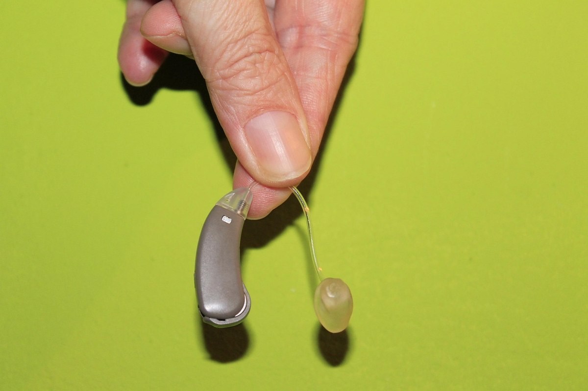 Main présentant un appareil auditif contour d'oreille gris avec tube auriculaire transparent sur fond jaune Main présentant un appareil auditif contour d'oreille gris avec tube auriculaire transparent sur fond jaune